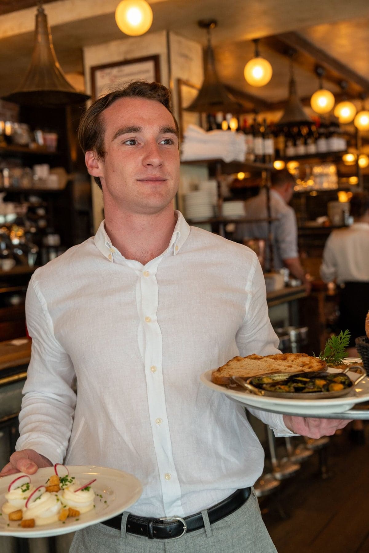 A waiter in a white shirt carries two plates