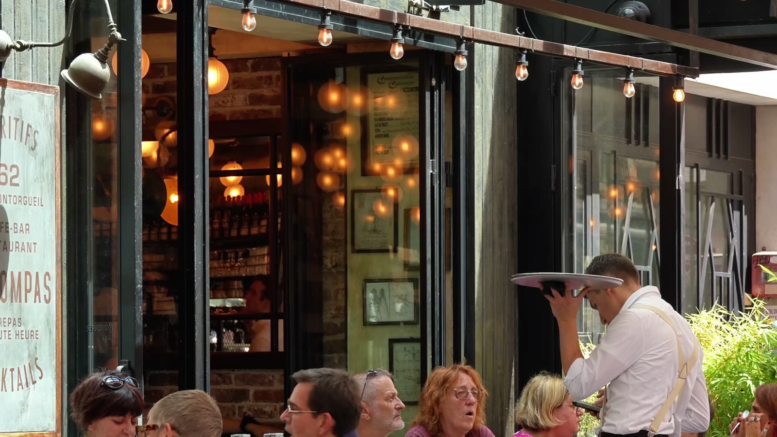 La terrasse du Compas en été : tables en rotin, guirlandes lumineuses et service en salle